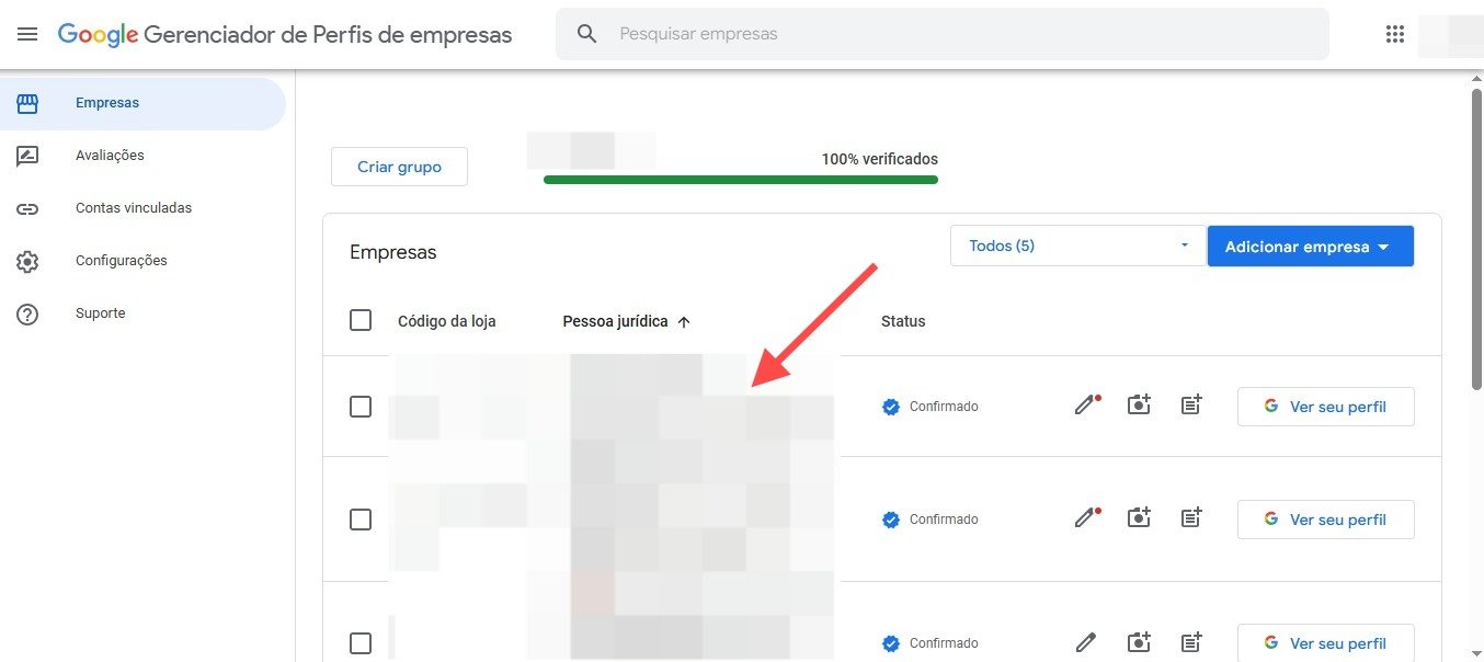 Captura de tela da interface do Google Gerenciador de Perfis de empresas em português, exibindo uma lista de negócios sob a seção "Empresas", com colunas para "Código da loja", "Pessoa jurídica" e "Status", além de ícones para edição e visualização de cada perfil. No topo da lista, há uma barra de progresso verde com o texto "100% verificados", indicando que todos os perfis foram confirmados. Uma seta vermelha aponta para uma das entradas, que está desfocada para preservar a privacidade. À esquerda, o menu de navegação inclui opções como "Empresas", "Análises", "Contas vinculadas", "Configurações" e "Suporte". No canto superior direito, há botões para "Criar grupo" e "Adicionar empresas", destacando funcionalidades de organização e expansão de perfis comerciais.