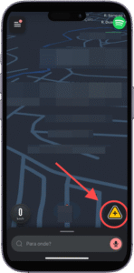 (Como cadastrar sua empresa no Waze). Captura de tela da interface de um aplicativo de navegação, o Waze, exibida em um smartphone, com mapa em modo escuro e linhas azuis representando vias. No canto inferior direito, há um ícone triangular amarelo com um ponto de exclamação, destacado por uma seta vermelha, indicando alerta ou perigo na rota. No canto inferior esquerdo, aparece o indicador de velocidade marcando "0 km/h", sugerindo que o usuário está parado. Ao centro, na parte inferior da tela, há uma barra de busca com o texto "Para onde?", permitindo ao usuário inserir um destino. A imagem destaca recursos de segurança e navegação em tempo real.