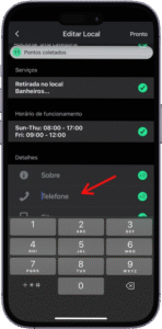 Captura de tela da interface de edição de local em um aplicativo móvel exibido em português, com o título "Editar Local" no topo. A tela apresenta três seções principais: "Serviços", com as opções "Retirada no local" e "Banheiros"; "Horário de funcionamento", exibindo os períodos "Sun-Thu: 08:00 - 17:00" e "Fri: 09:00 - 12:00"; e "Detalhes", com ícones para "Sobre", "Telefone" — este destacado por uma seta vermelha — e outro campo não especificado. A parte inferior da tela mostra um teclado numérico com os dígitos de 0 a 9 e letras correspondentes, indicando que o usuário está inserindo ou editando o número de telefone do estabelecimento. A imagem representa a personalização de dados comerciais em uma plataforma de mapeamento ou perfil empresarial.
