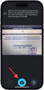 Captura de tela da interface de câmera de um smartphone, provavelmente do aplicativo Waze, com instruções em português no topo dizendo: "Adicione uma foto deste local para outros Wazers. Ela aparecerá publicamente com seu nome de usuário e será utilizada em outros serviços do Google." No visor da câmera, aparece uma apresentação com o texto "COMO SERIA SE O GOOGLE FOSSE O MAIOR VENDEDOR DA SUA EMPRESA?" e a imagem de uma pessoa em chamada de vídeo. Na parte inferior da tela, há três ícones: galeria à esquerda, botão de captura ao centro — destacado por uma seta vermelha — e alternância de câmera à direita. A imagem sugere a funcionalidade de registrar e compartilhar locais com outros usuários da plataforma.